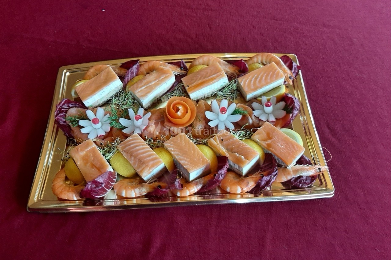 Plateau de saumon, crevettes, tranches de citron et décorations florales comestibles sur une nappe rouge.