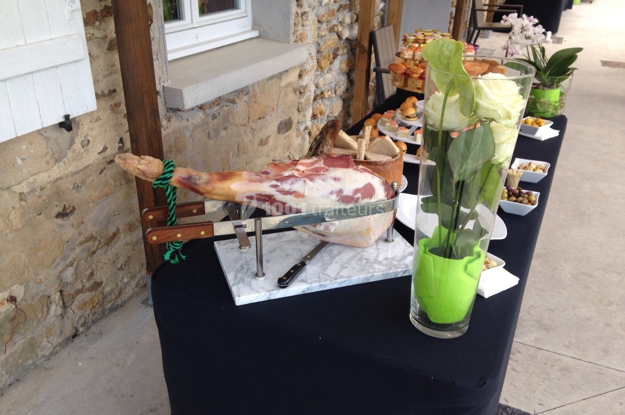 Jambon sur un support avec couteaux, disposé sur une table garnie de fleurs et d'amuse-bouches en extérieur.