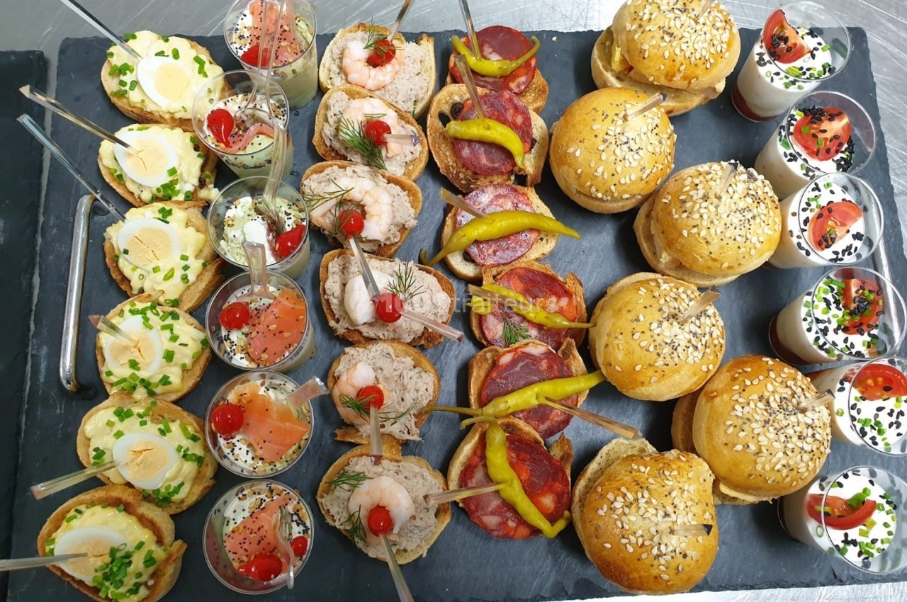 Plateau de bouchées variées comprenant mini-burgers, verrines, toasts garnis et charcuterie sur une ardoise noire.