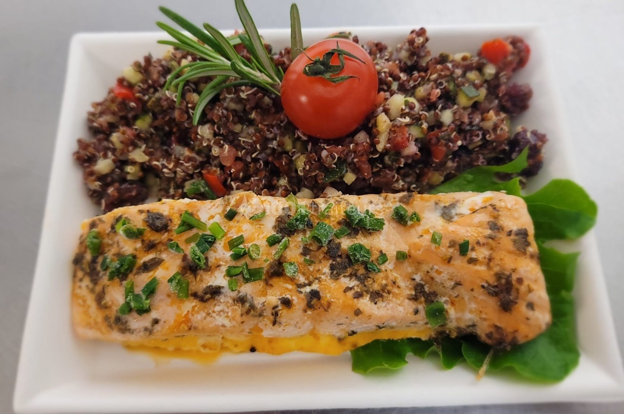 Filet de saumon grillé garni de ciboulette, accompagné de quinoa aux légumes et d'une tomate cerise sur un lit de salade.