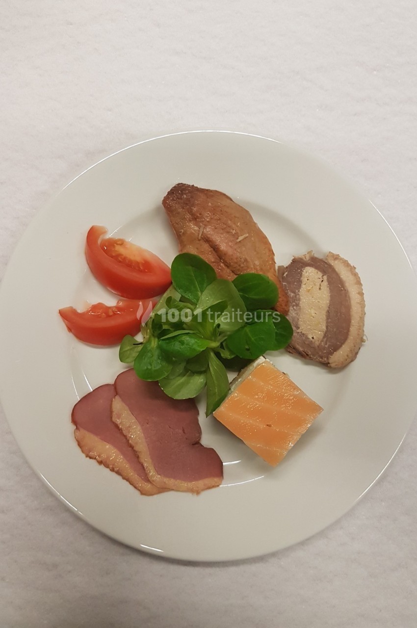 Assiette contenant du magret de canard fumé, du saumon, une tranche de pâté, de la mâche et des quartiers de tomate.