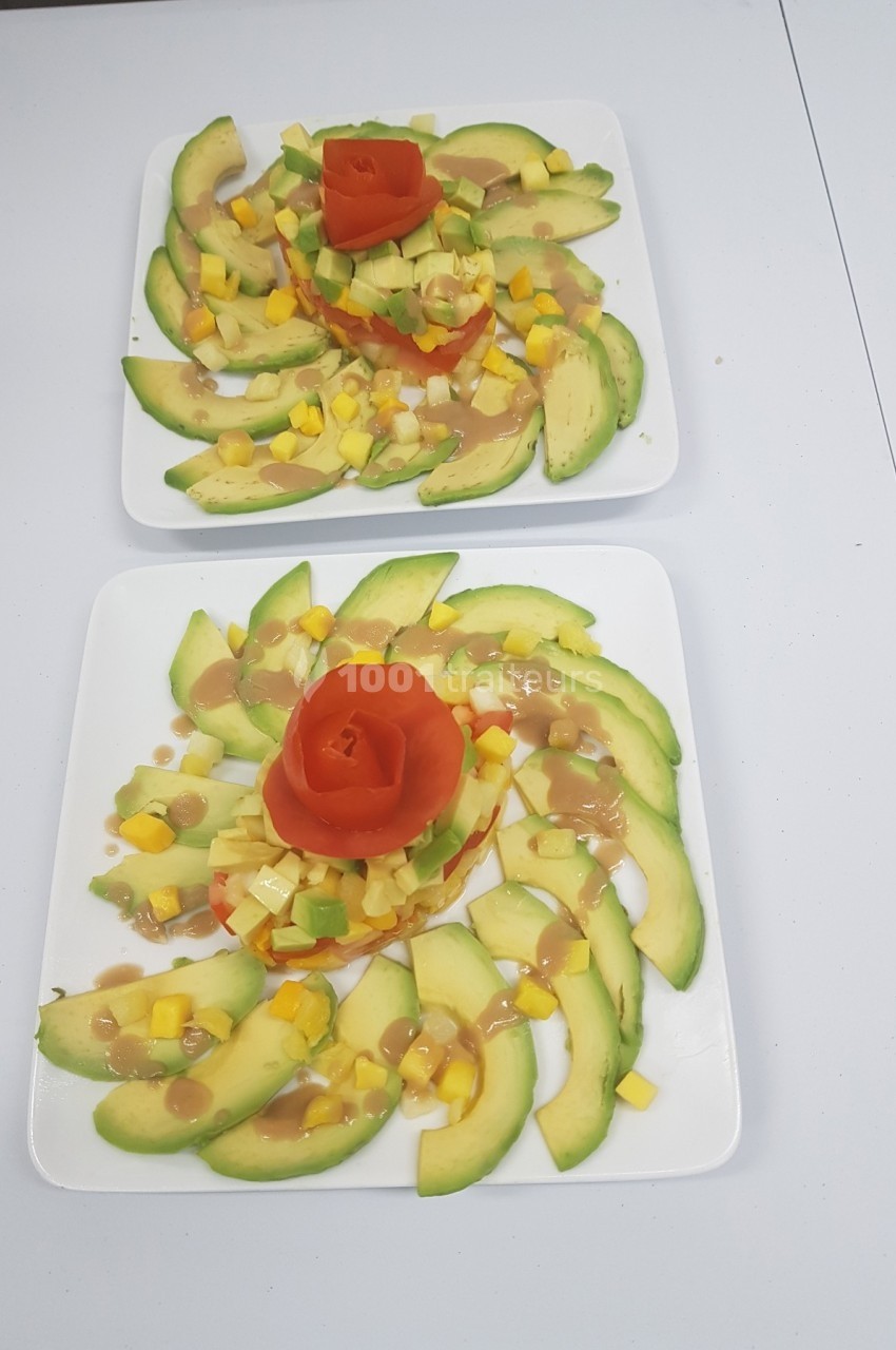Assiettes garnies de tranches d'avocat, dés de mangue et tomate sculptée, disposées en présentation artistique.