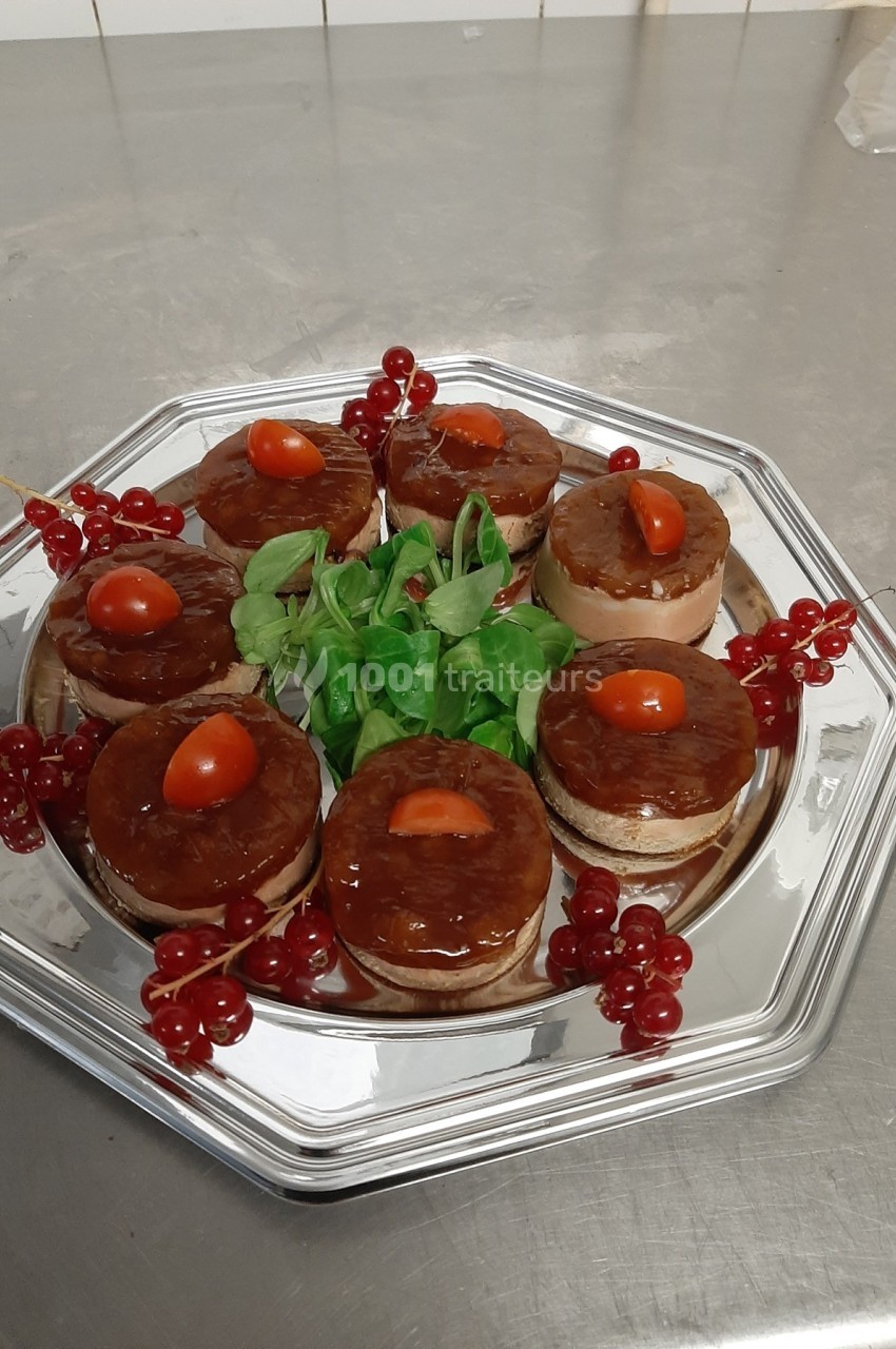 Plateau en métal avec des bouchées garnies de gelée, tomates cerises, groseilles et feuilles vertes en décoration.