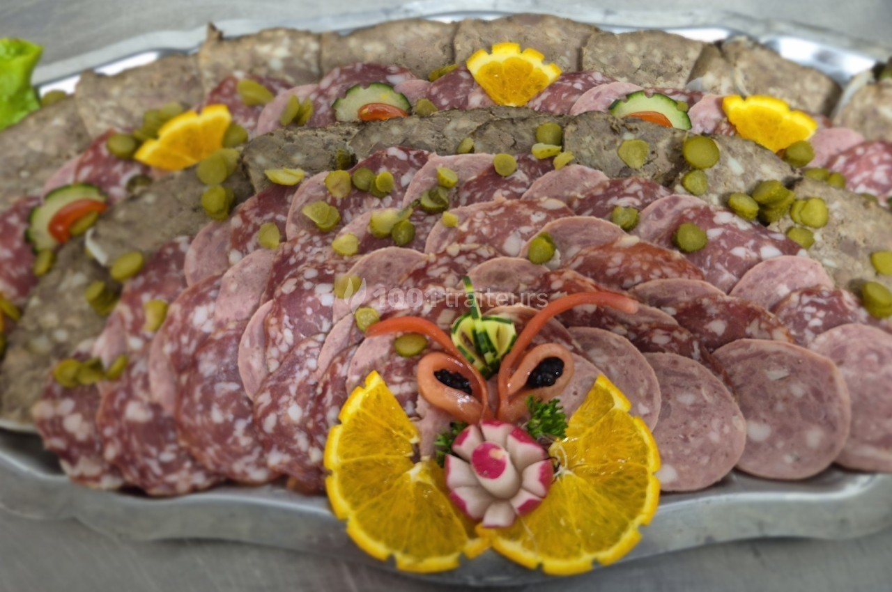 Plateau de charcuterie variée avec rondelles de cornichons, tranches d'orange et décoration de légumes.