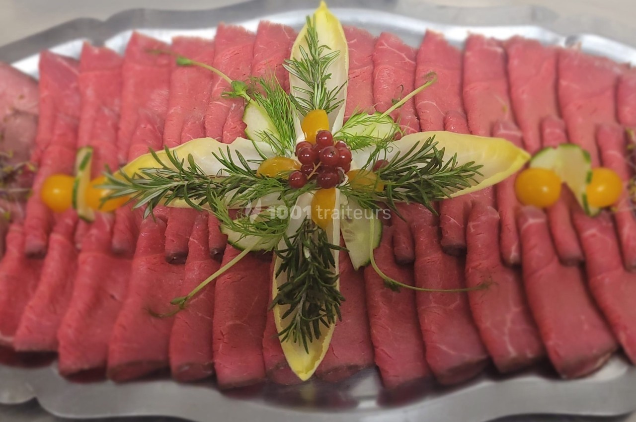 Plateau de tranches de rôti de bœuf disposées en éventail, décoré de feuilles d'endive, herbes et baies rouges.