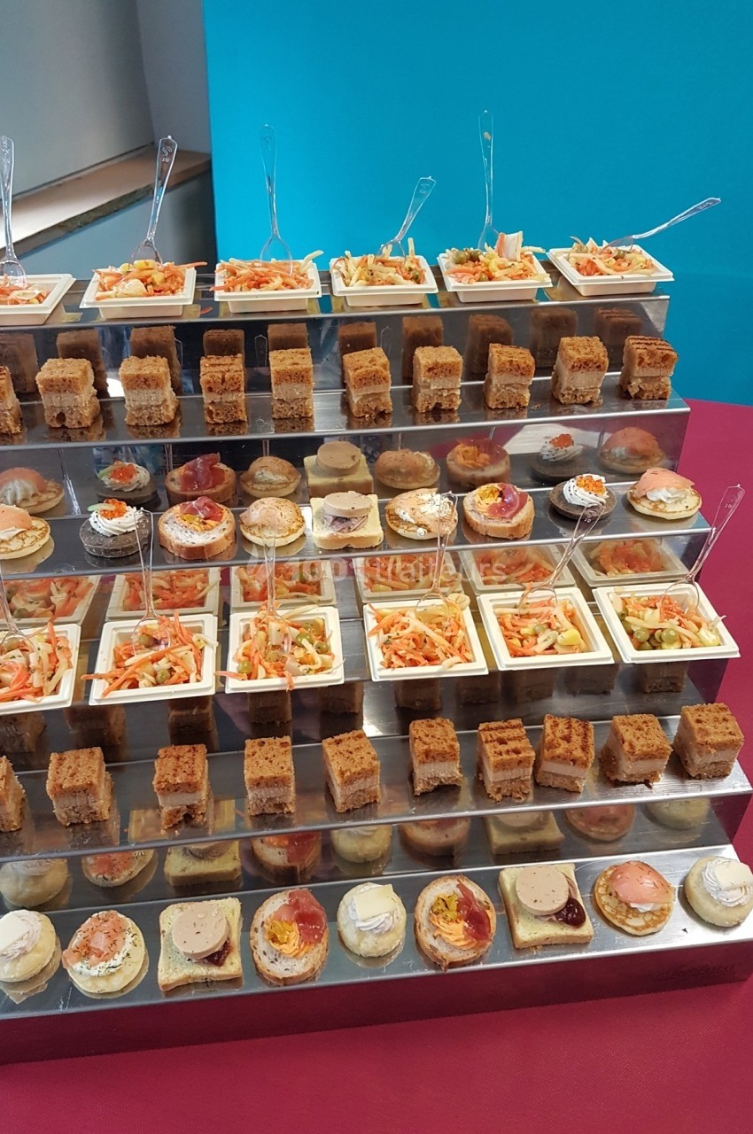 Plateau de présentation avec plusieurs étages de bouchées salées variées, disposées sur une table rose.