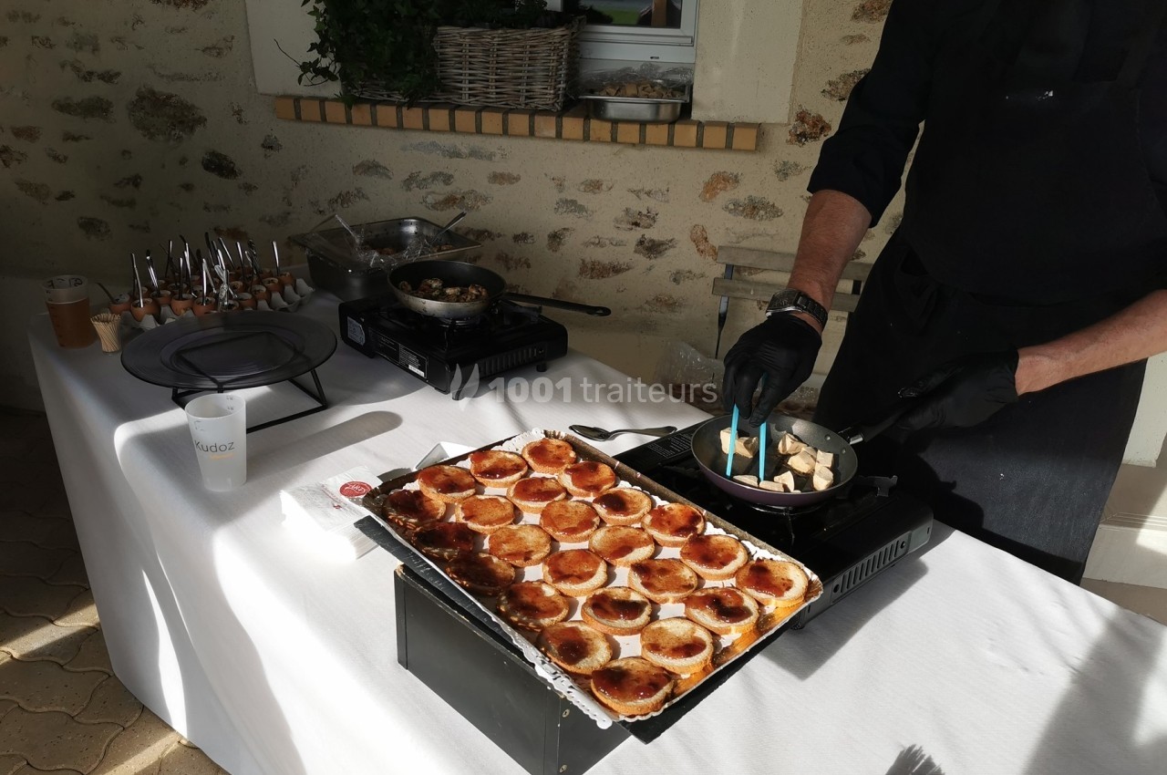 Un cuisinier prépare des plats sur une table blanche avec des mini-tartelettes et des champignons sautés.
