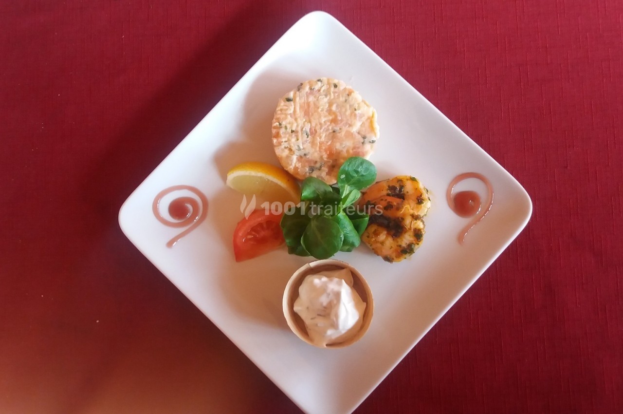 Assiette dressée avec un tartare, une garniture de légumes, une sauce en ramequin et une décoration sur nappe rouge.