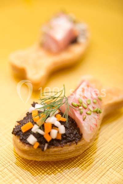 Bouchée en forme de poisson garnie de tapenade, dés de légumes, saumon et aneth sur une nappe dorée.