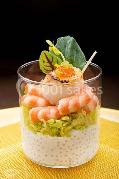 Verrine composée de crevettes, noix de Saint-Jacques, perles de tapioca et salade, présentée sur une nappe jaune.