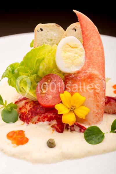 Plat gastronomique composé de chair de crabe, salade, œuf dur, tomate, fleur comestible et sauce crémeuse.