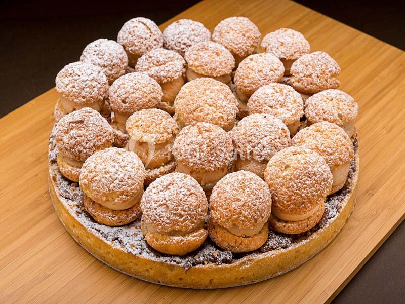 Plateau de choux à la crème saupoudrés de sucre glace, disposés sur une base en pâte sur une planche en bois.