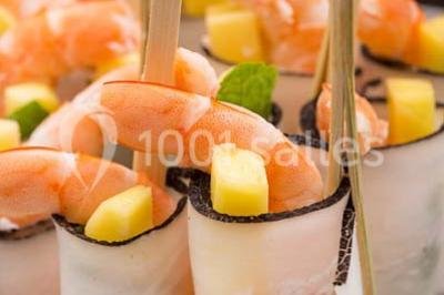 Dessert au chocolat brillant orné de feuille d'or, posé sur une base avec éclats de cacao, sur fond sombre.