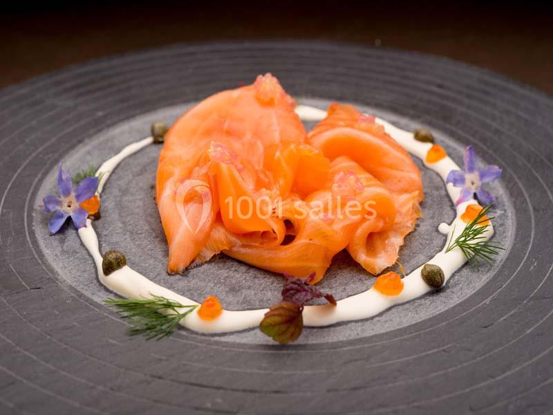 Tranches de saumon fumé disposées sur une assiette avec crème, câpres, œufs de poisson et décorations florales.