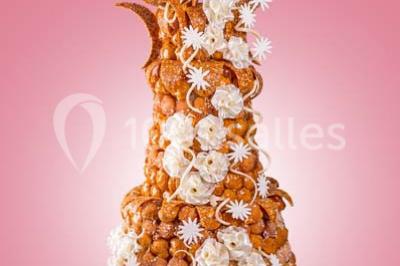 Dessert au chocolat brillant orné de feuille d'or, posé sur une base avec éclats de cacao, sur fond sombre.