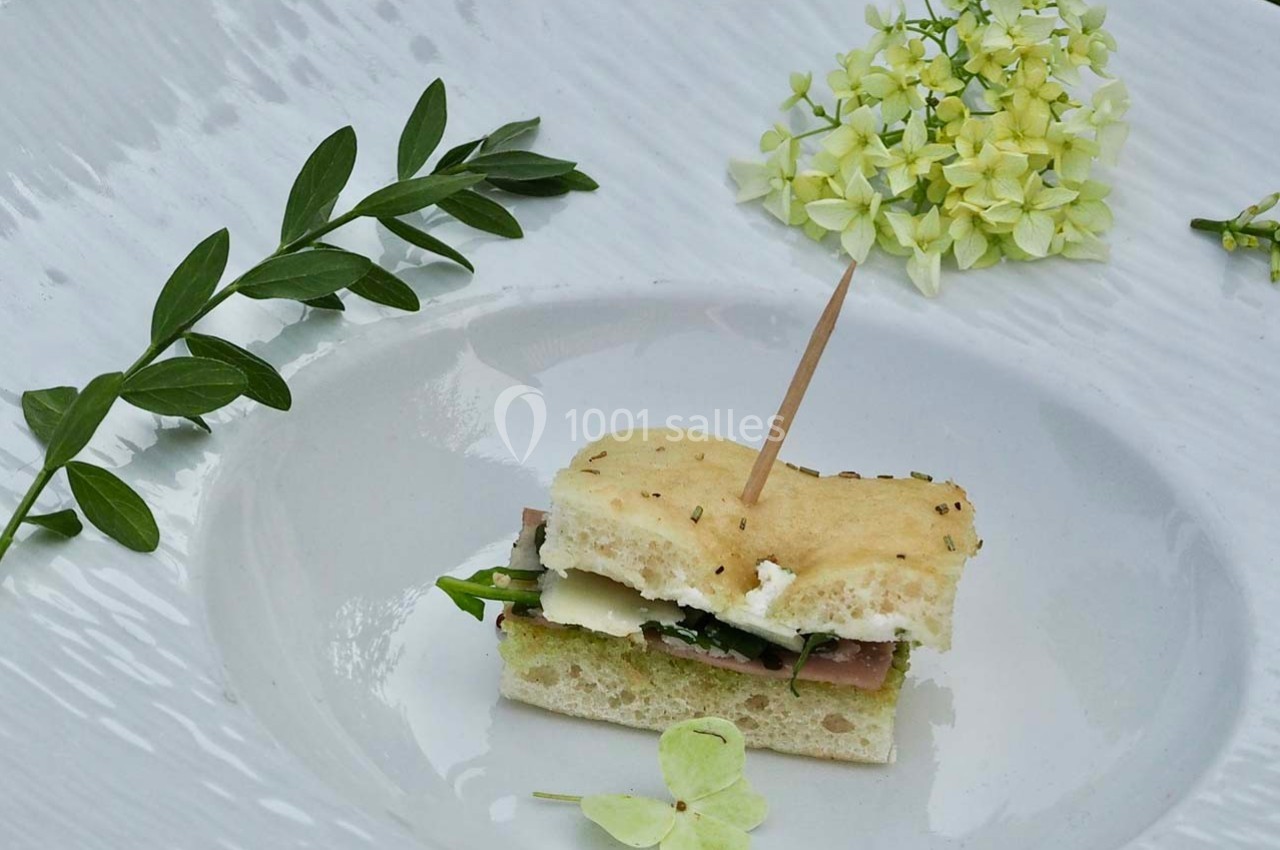 Mini sandwich garni de jambon, fromage et roquette, présenté sur une assiette blanche avec des fleurs décoratives.