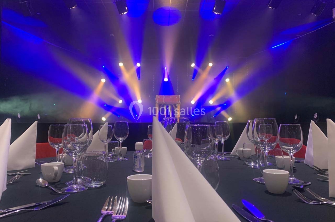 Salle de réception avec tables dressées et éclairage coloré de scène en arrière-plan.