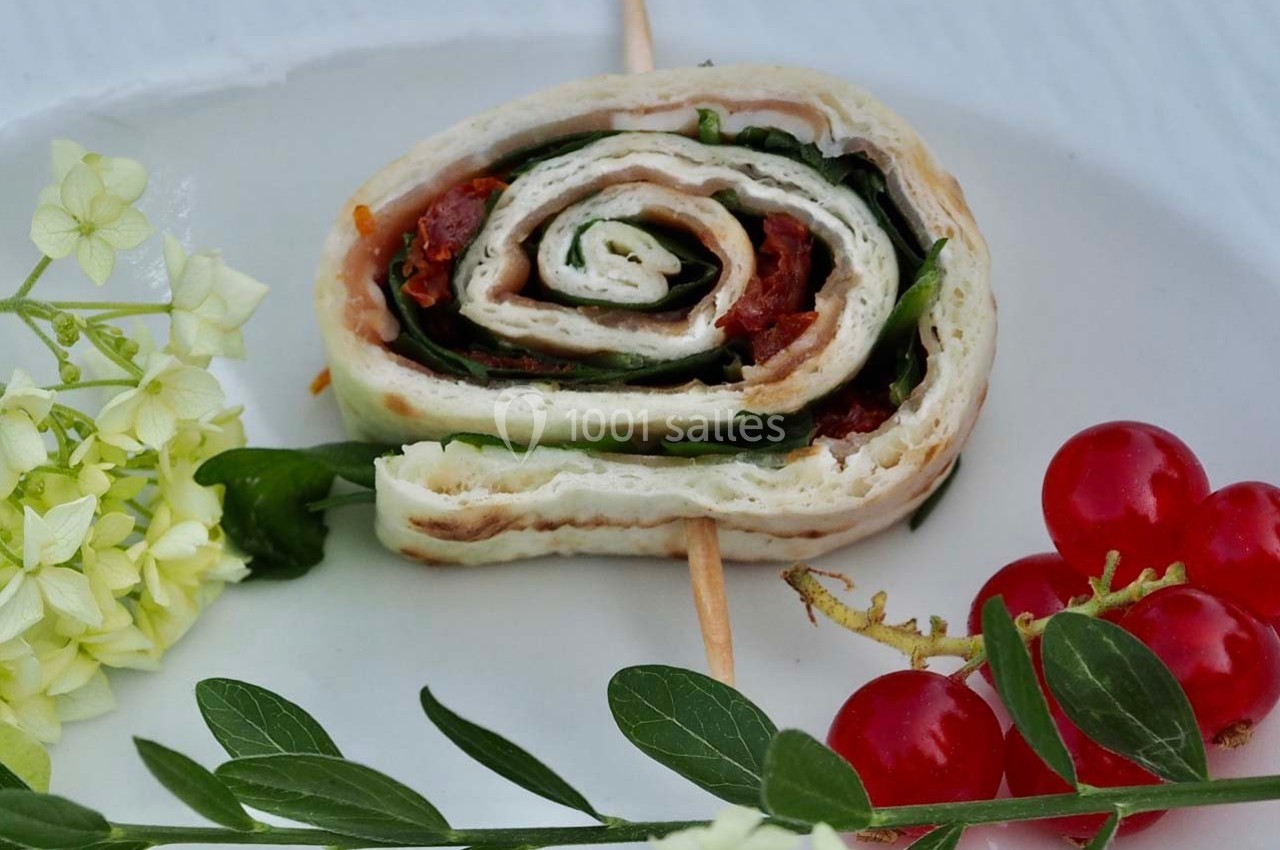 Roulé de tortilla garni de légumes et épinards, présenté sur une assiette avec fleurs et tomates cerises.