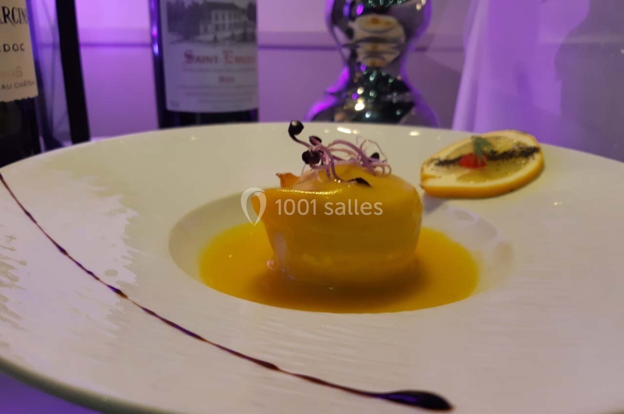 Dessert élégant présenté dans une assiette blanche, nappé de sauce jaune, décoré de micro-pousses et d'une tranche d'orange.