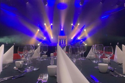 Salle de réception éclairée en bleu avec des tables rondes dressées et des écrans disposés autour.