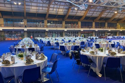 Salle de réception éclairée en bleu avec des tables rondes dressées et des écrans disposés autour.