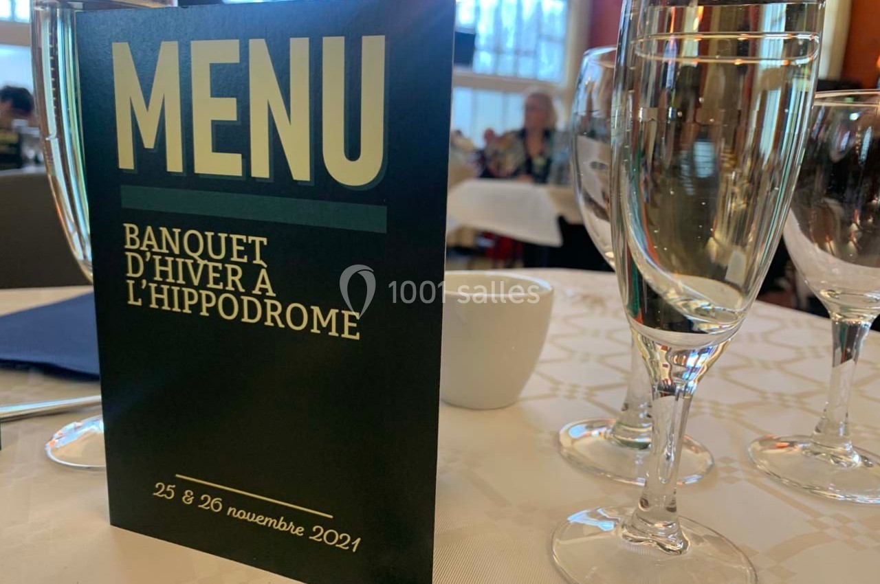 Carte de menu pour un banquet d'hiver à l'hippodrome, posée sur une table avec des verres et une nappe blanche.