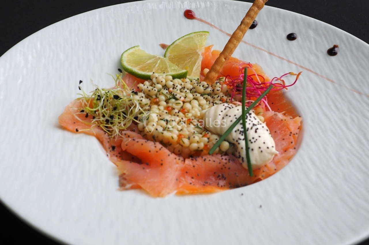 Assiette de saumon fumé avec crème, salade de perles, citron vert, grissini et décoration colorée.