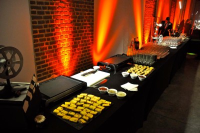 Salle de réception éclairée en bleu avec des tables rondes dressées et des écrans disposés autour.