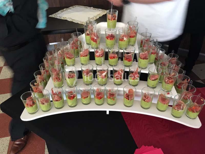 Présentoir avec plusieurs verrines contenant une mousse verte garnie de morceaux de jambon et de légumes.