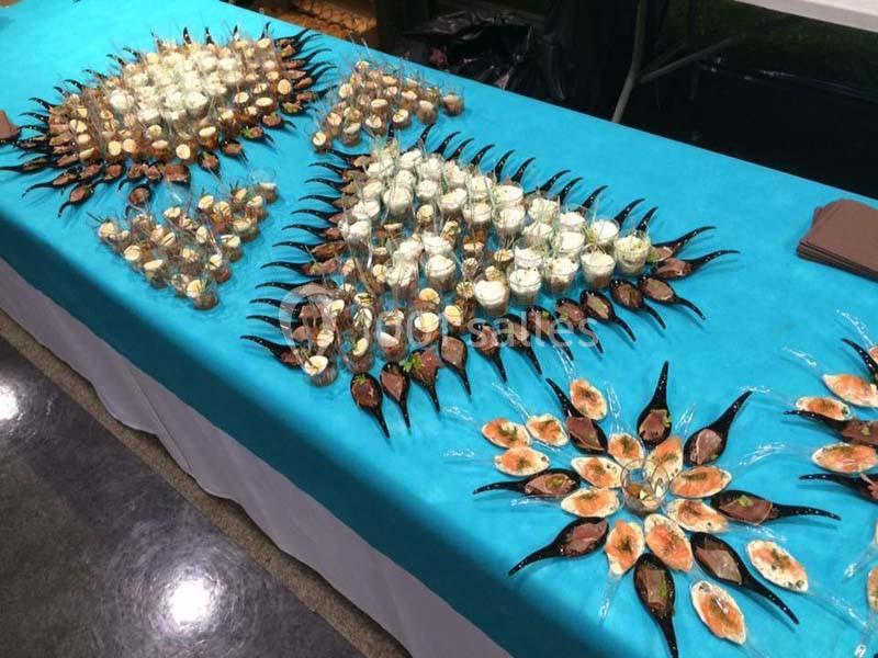 Présentation soignée de verrines et amuse-bouches sur une nappe bleue, disposés en motifs géométriques.