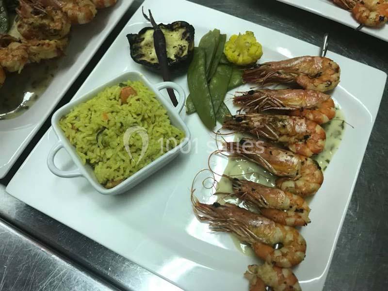 Assiette composée de crevettes grillées, riz épicé, légumes vapeur et aubergine grillée, servie sur un plateau blanc.