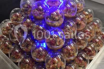 Table décorée pour un dîner, avec nappes blanches, serviettes pliées, lanternes, fleurs et couverts disposés.