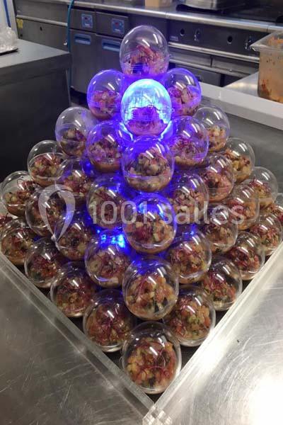 Pyramide de sphères transparentes contenant des portions de salade, éclairée par une lumière bleue au centre.