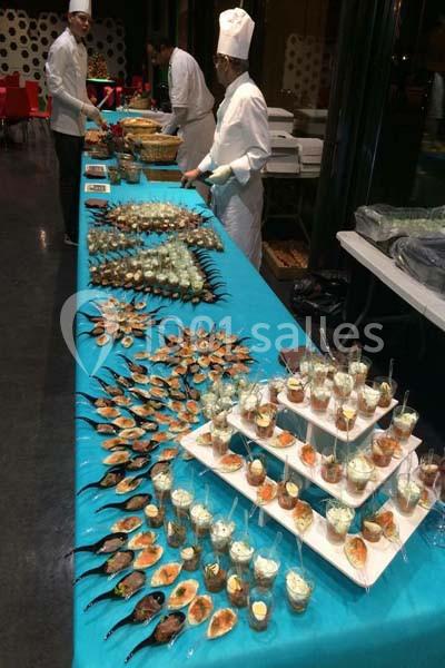 Buffet de réception avec des chefs en arrière-plan et une variété de plats présentés sur une table turquoise.