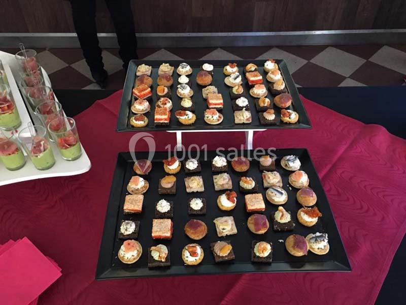 Plateaux de canapés variés disposés sur une nappe rouge, avec verrines en arrière-plan.