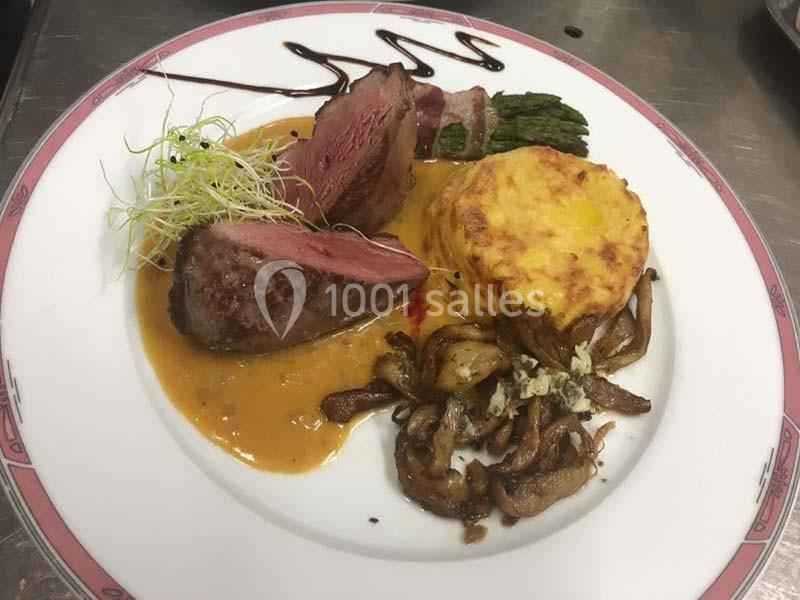 Assiette composée de viande rouge, gratin, asperges, champignons sautés et sauce, dressée avec soin.