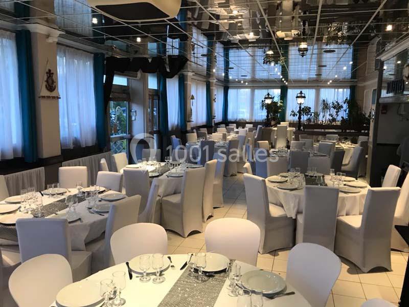 Salle de réception lumineuse avec tables rondes dressées, nappes blanches et chaises assorties.