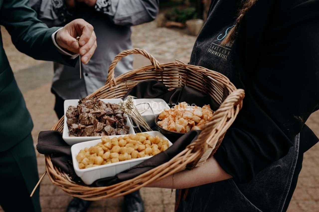 Un panier en osier contenant des plats de viande, crevettes et croûtons, tenu par une personne en uniforme.