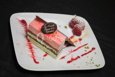 Dessert raffiné composé d'une mousse rose, d'une sauce rouge en verrine et d'un carré de chocolat décoratif.