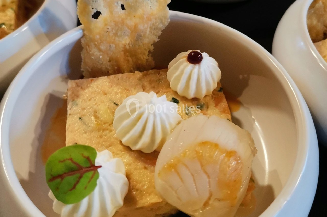 Portion de terrine garnie de noix de Saint-Jacques, crème décorative, feuille verte et tuile croustillante.