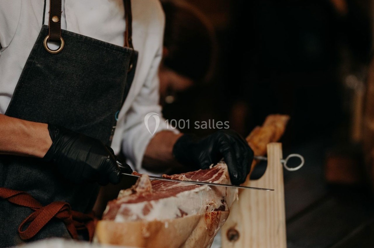 Un cuisinier en tablier tranche délicatement un jambon posé sur un support en bois.