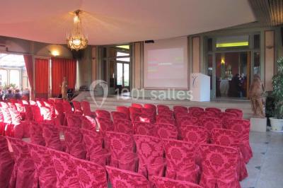 Salle de réception éclairée de lumières violettes, avec un bar, des tables hautes et des rideaux rouges.
