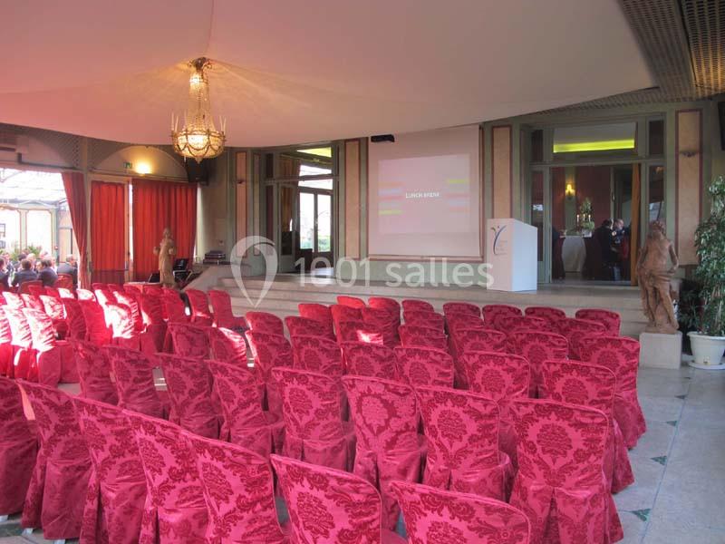 Salle de conférence avec des rangées de chaises rouges face à une scène équipée d'un écran de projection.