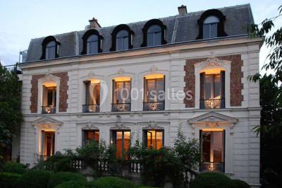 Salle de réception éclairée de lumières violettes, avec un bar, des tables hautes et des rideaux rouges.