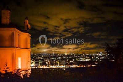 Salle de réception éclairée de lumières violettes, avec un bar, des tables hautes et des rideaux rouges.