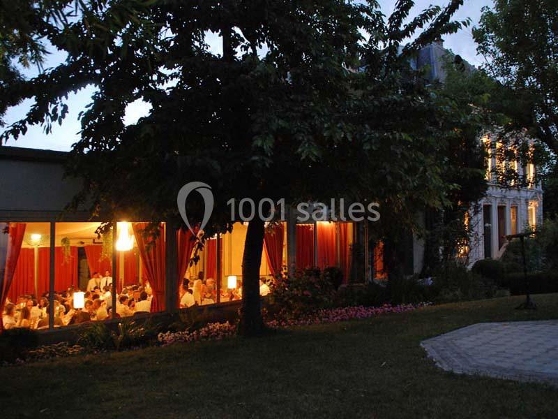 Vue extérieure d'un restaurant éclairé en soirée, avec des convives visibles à travers de grandes baies vitrées.