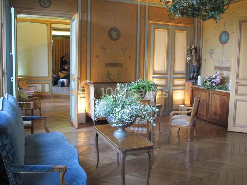 Salon élégant avec parquet en bois, mobilier classique, fleurs fraîches et murs décorés de motifs anciens.