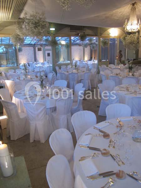 Salle de réception décorée avec des tables rondes dressées, nappes blanches et chaises assorties.