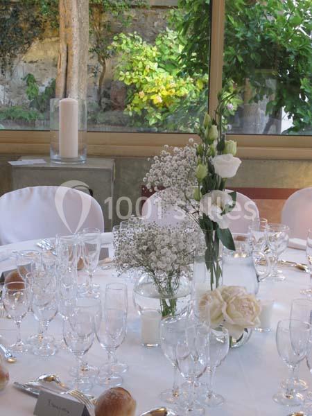 Table élégamment dressée avec nappes blanches, verres, bougies et centre de table floral dans un cadre lumineux.