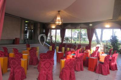 Salle de réception éclairée de lumières violettes, avec un bar, des tables hautes et des rideaux rouges.